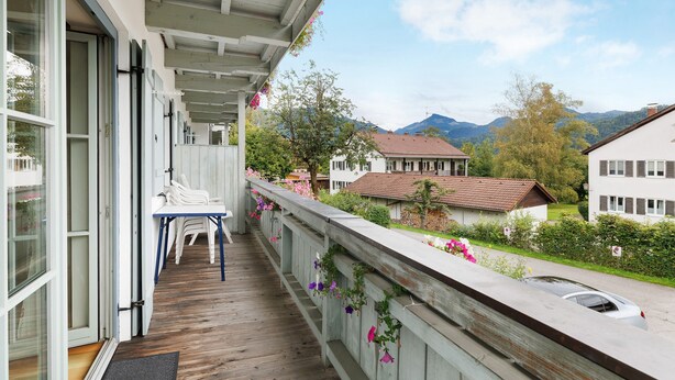 A wooden deck with a table and chairs, overlooking a residential area with houses and mountains. - Apartment 'Fewo Brünnstein- Nr 28 Pool, Sauna' with Mountain View, Shared Garden & Wi-Fi (Oberaudorf)
