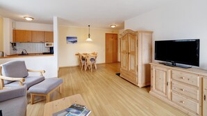 A living room with a TV, wooden furniture, and a dining area with chairs and a table. - Apartment 'Fewo Brünnstein- Nr 28 Pool, Sauna' with Mountain View, Shared Garden & Wi-Fi (Oberaudorf)
