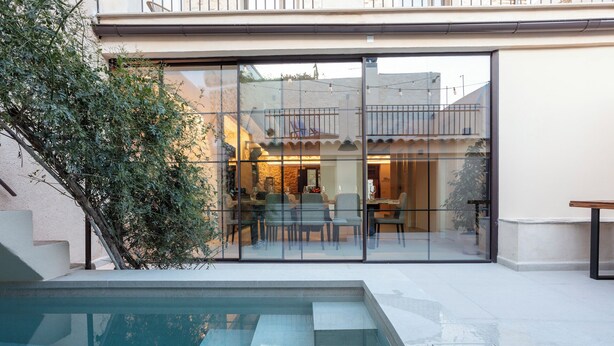 Una casa moderna con un patio con paredes de vidrio, una piscina y un comedor visible a través del vidrio.