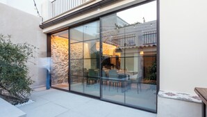 Un patio con cerramiento de vidrio, un muro de piedra y una zona de comedor con sillas y mesas.