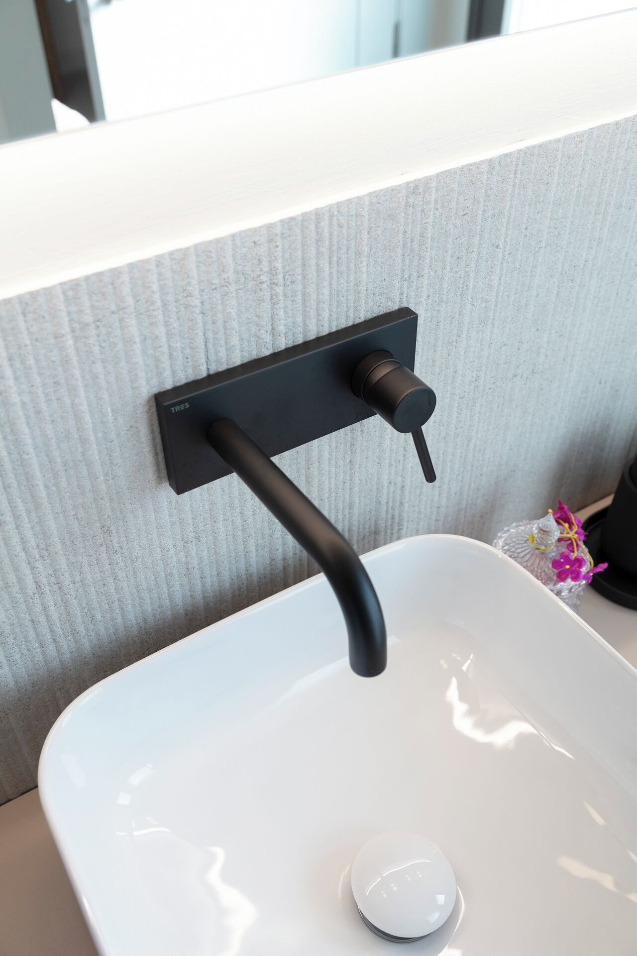 A modern bathroom with a white sink, a black faucet, and a textured wall.