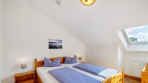 A bedroom with a sloped ceiling, a skylight, a bed with checkered bedding, a bedside table with a lamp, and a small painting on the wall. - Apartment 'Brünnstein Room 60' with Mountain View, Shared Garden & Wi-Fi (Oberaudorf)