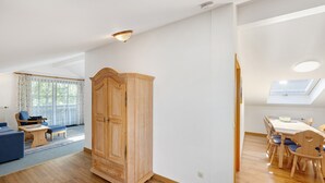 A spacious living area with a wooden wardrobe, a dining table with chairs, and a skylight. - Apartment 'Brünnstein Room 60' with Mountain View, Shared Garden & Wi-Fi (Oberaudorf)