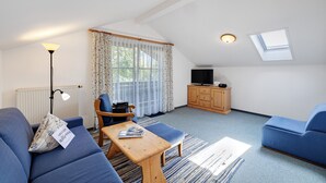 A modern living room with a sofa, a wooden coffee table, a television, and a ceiling window. - Apartment 'Brünnstein Room 60' with Mountain View, Shared Garden & Wi-Fi (Oberaudorf)
