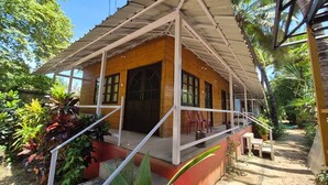 A wooden house with a porch, surrounded by lush greenery. - Furtados Beach Cottages  (Benaulim)