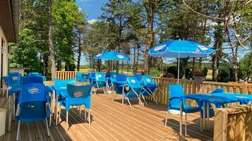 Terraza al aire libre con sillas y mesas azules, rodeada de árboles.