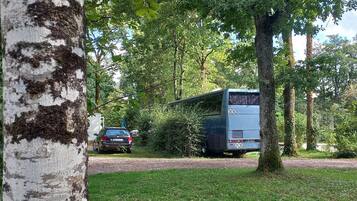 Un autobus est garé dans une zone boisée, avec une voiture en arrière-plan.