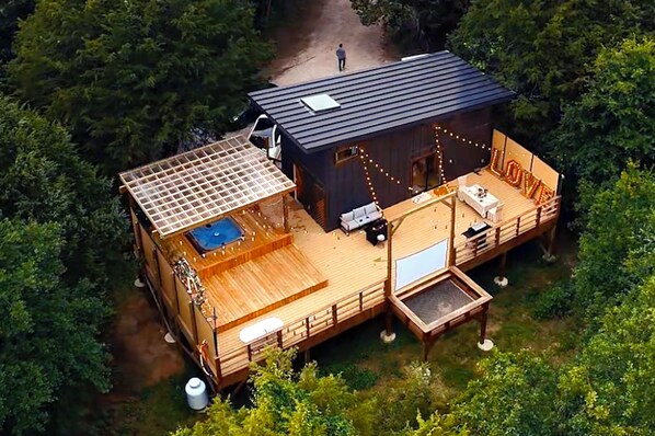 A cabin with a deck, a hot tub, and a covered outdoor seating area. - NestScape–-Stargaze from Bed + Outdoor Tub & Movie (Wills Point)