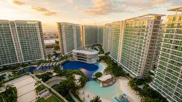 A high-rise hotel with multiple balconies, a central swimming pool, and lush greenery.