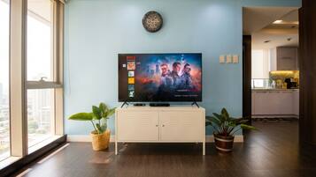 A modern living room with a flat-screen TV mounted on a wall, a white cabinet below, and two potted plants.
