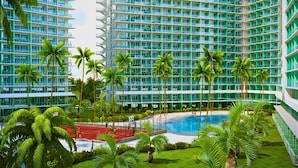Un hotel moderno de gran altura con varios balcones, una piscina central y abundante vegetación.