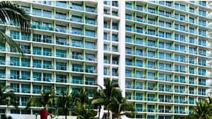 Un hotel frente a la playa con piscina, palmeras y un parque infantil.
