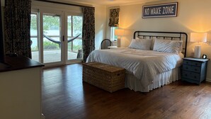 Ein Schlafzimmer mit Bett, Nachttisch, Lampe, einer Wandtafel und Blick ins Freie durch eine Schiebetür.