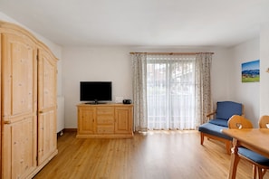 Ein Zimmer mit einem Holzkasten, einem Fernseher, einem blauen Sessel und einem Tisch.