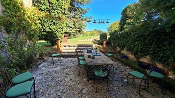 Un patio al aire libre con suelo de piedra, una mesa con sillas y una guirnalda de luces.