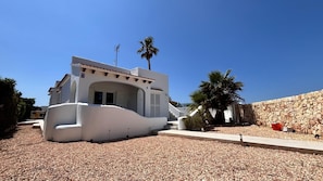 A modern white building with a curved facade, a stone wall, and a palm tree.