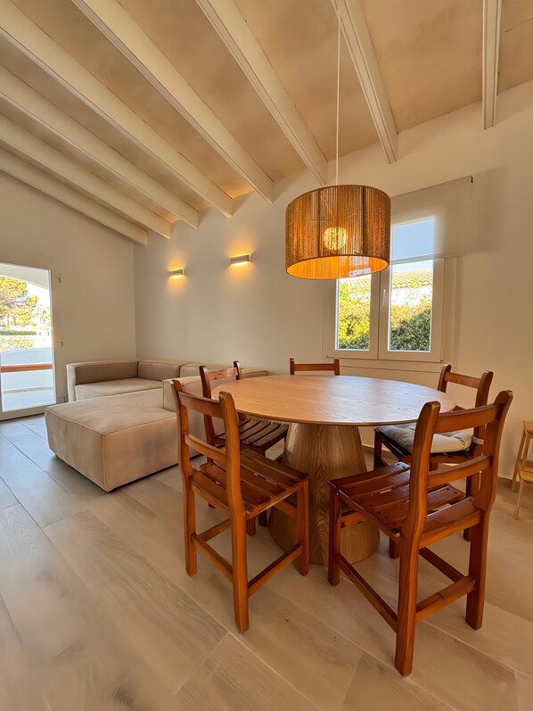 A spacious dining area with a round wooden table, six wooden chairs, a large pendant light, and a built-in bench.