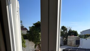 A view through a sliding glass door to a swimming pool with clear water, a tiled deck, and a stone wall.