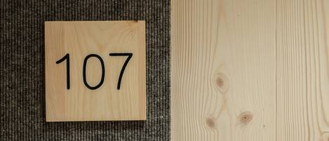 A wooden sign with the number 107 on a carpeted floor next to a wooden wall.