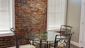 A dining area with a glass table surrounded by metal chairs, a brick wall, and wooden flooring. - Repurposed space upstairs on LaFayette Square (LaFayette)