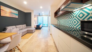 A modern kitchen with a patterned backsplash, a dining area with a wooden table and chairs, a gray sofa, and a view to a balcony. - Comfortable studio with pool and gym - Huaya 101 (Playa del Carmen)