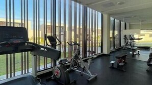 Een fitnessruimte met cardioapparatuur, een loopband en een hometrainer.