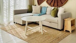 Een moderne woonkamer met een beige bank, een rond bijzettafeltje en een groot wandkunstwerk van geweven materiaal.