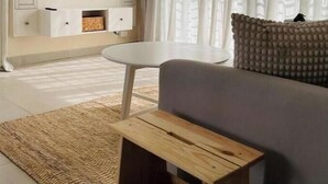 Een woonkamer met een flatscreen televisie aan de muur, een klein rond tafeltje, een bank en een decoratief vloerkleed.