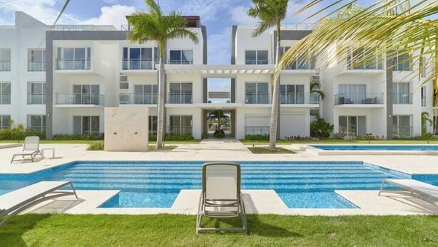 A modern hotel with a central pool, palm trees, and a clear sky. - Garden View Relaxing Retreat (Punta Cana)
