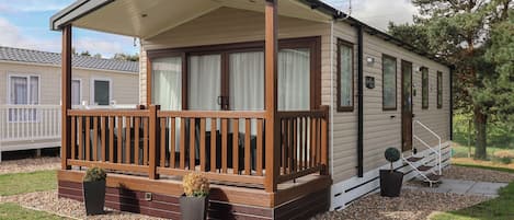 A mobile home with a covered porch, two potted plants, and a small staircase leading to the entrance.