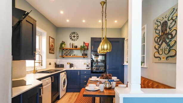 Une cuisine moderne avec des meubles de couleur bleu foncé, une table à manger en bois et un luminaire suspendu.