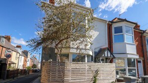 Un immeuble résidentiel au design moderne, avec un arbre remarquable dans le jardin avant et une clôture en bois.