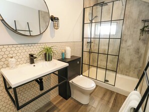 Ein Badezimmer mit Waschbecken, Toilette, Duschkabine mit Glastür, Topfpflanze und Spiegel.