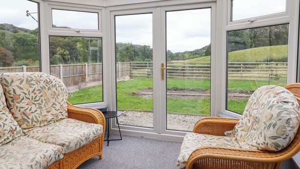 A conservatory with wicker furniture and a view of a green landscape.