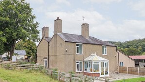 A two-story house with a conservatory, a fenced yard, and a hill in the background.