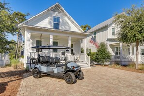 Una casa bianca con veranda, un golf cart parcheggiato davanti e una bandiera americana su un lato.