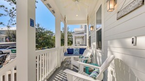 A covered porch with white railings, a ceiling fan, and a sign reading "Life is Good at the Beach".