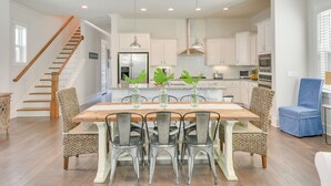 A spacious kitchen with white cabinetry, a wooden dining table with metal chairs, and a staircase with wooden railings.