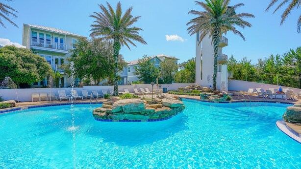 A swimming pool with lounge chairs, palm trees, and a building in the background.