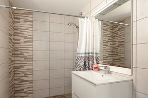 Een douche met een glazen deur, een zeepdispenser en een spiegel boven de wastafel.