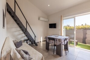 Un salon moderne comprenant un canapé, une table à manger, un escalier et une grande porte-fenêtre coulissante donnant sur un jardin.