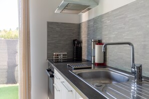Een moderne keuken met een roestvrijstalen spoelbak, een inbouwafzuigkap en een grijze betegelde achterwand.