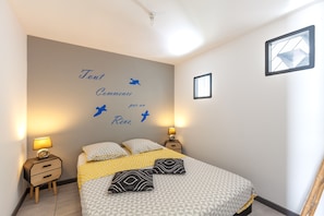 A bedroom with a bed, two bedside tables, a wall with a decorative phrase, and a window. - Holiday Home 'Mexico' with Balcony and Air Conditioning (Saint-Mitre-les-Remparts)