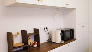 A kitchen with white cabinets, a microwave, a coffee maker, and a wooden shelf with a chair. - Pleasant stay in the heart of Paris, 4 people max (Paris)