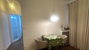 A room with a wooden floor, a green table with a patterned tablecloth, a chair, a hanging light fixture, a door with frosted glass panels, and a radiator. - Pleasant stay in the heart of Paris, 4 people max (Paris)