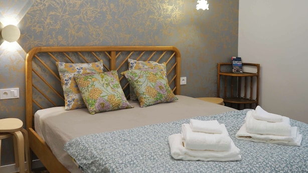 A neatly made bed with floral pillows, a bedside table with a book, and a wall-mounted light fixture. - Pleasant stay in the heart of Paris, 4 people max (Paris)