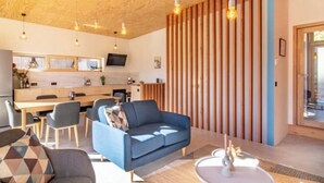 Una sala de estar moderna con un sofá azul, una mesa de comedor y sillas. Se observa una pared de listones de madera y un televisor montado sobre la mesa.