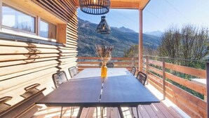 Una terraza de madera con una mesa y sillas, un jarrón con flores secas y vistas a la montaña.