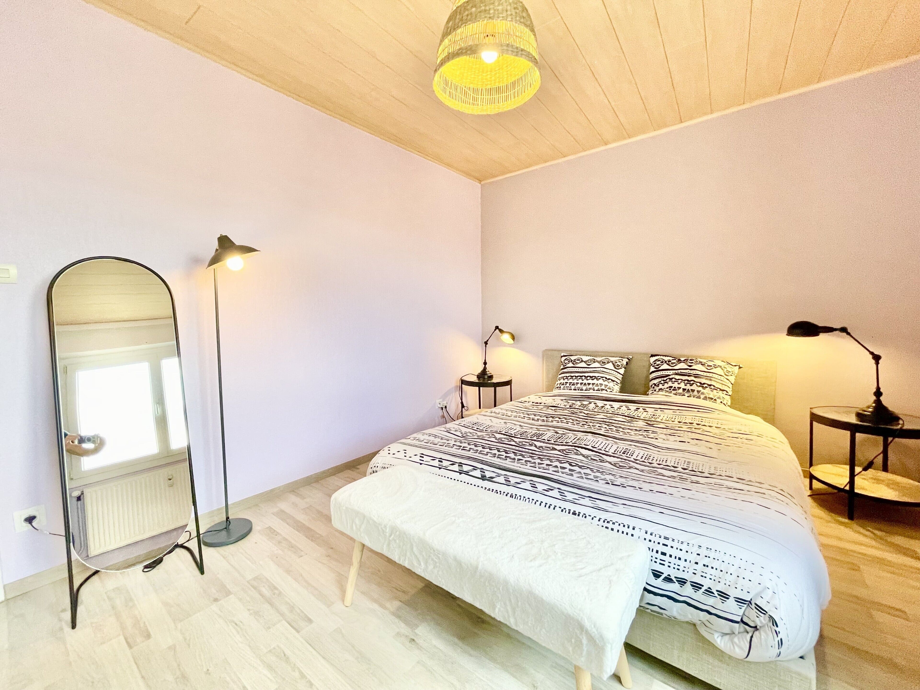 Une chambre à coucher comprenant un lit, des lampes de chevet, une lampe sur pied, un miroir et un luminaire au plafond.