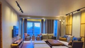 A modern hotel room with a large window offering a mountain view, a flat-screen TV, and a cozy seating area with ottomans and chairs. - the perch shimla (Shimla)